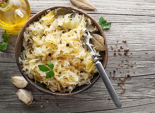 Homemade sauerkraut with black pepper and parsley in wooden bowl on rustic background. Top view. Copy space.