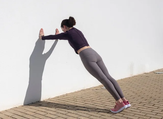 Sporty woman doing press ups against a white wall outside.