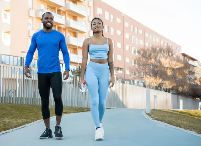 Healthy lifestyle concept. Dark-skinned millennial couple doing outdoor sports together, the man and woman walk through a park in autumn, the black girl with braids carries a bottle of water.