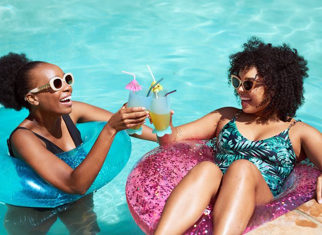 Two friends cheers and clink fancy mocktails in the pool, swimming inflatables