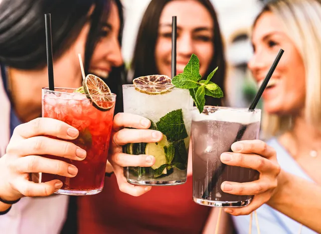 Group of happy friends toasting and drinking fancy cocktails at bar terrace-Three Young girls drink mojito and clinking glass together at pub enjoying happy hour at summer party- Life Style concept