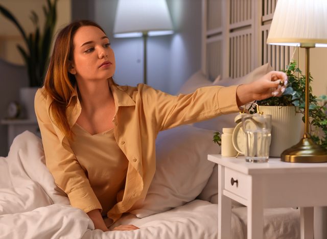 Young woman turning off lamp before sleep in bedroom