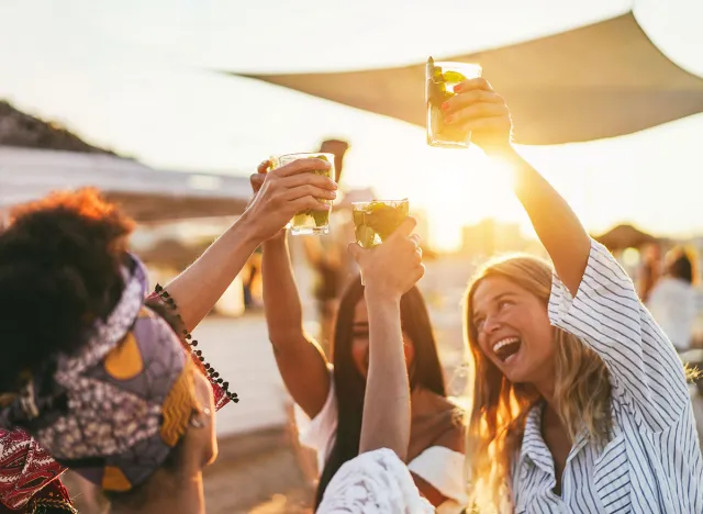 Multiracial happy friends cheering and drinking mojitos at beach party - Focus on left hand holding cocktail