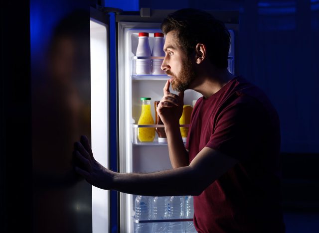 Man choosing food from refrigerator in kitchen at night. Bad habit