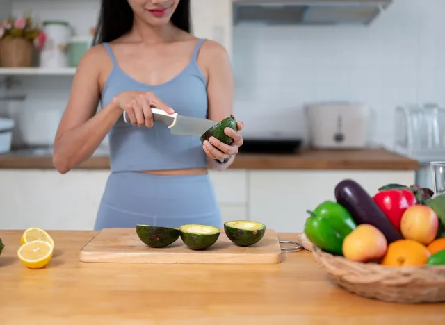 Cropped image of a beautiful and fit Asian woman in gym clothes cutting an avocado and preparing her healthy breakfast in the kitchen before going to the gym.