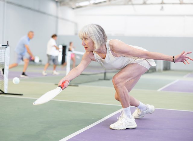 Mature adult woman playing doubles pickleball game, healthy lifestyle concept