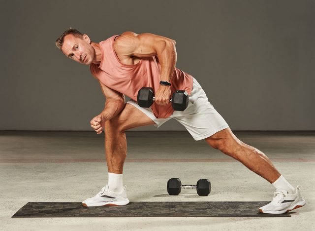 one-arm dumbbell row in a bent-over position with emphasis on the leg by a handsome Caucasian athlete in shorts and a T-shirt. fitness. aerobics. exercises on the mat. physical health