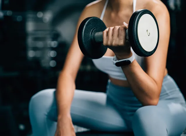 A fitness enthusiast training at the gym, lifting weights and performing exercises with dumbbells to build up her strength and maintain her health and beauty, fitness GYM dark background