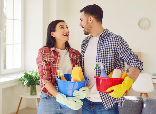 Happy couple, armed with cleaning equipment, bringing joy to the living room. Family showing fun teamwork and shared responsibility, where household chores become moments of connection.