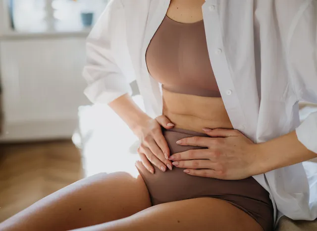 Woman at home suffering from menstrual pain, having cramps. Close up of woman holding abdomen, endometriosis, and conditions causing pain in tummy.