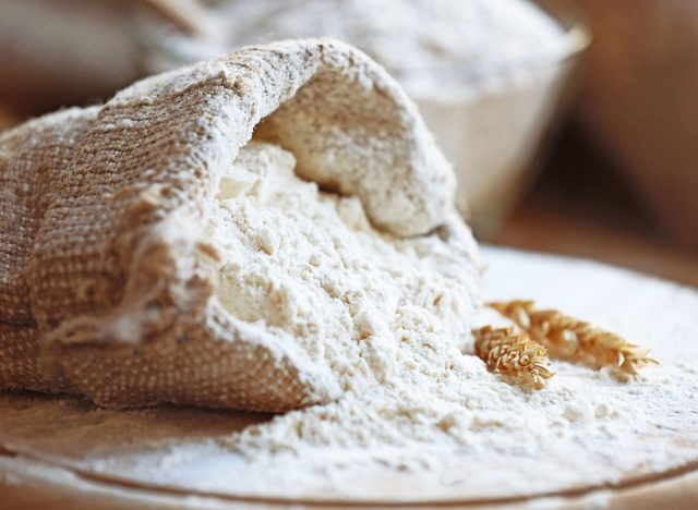 Flour in burlap bag on cutting board and wooden table background