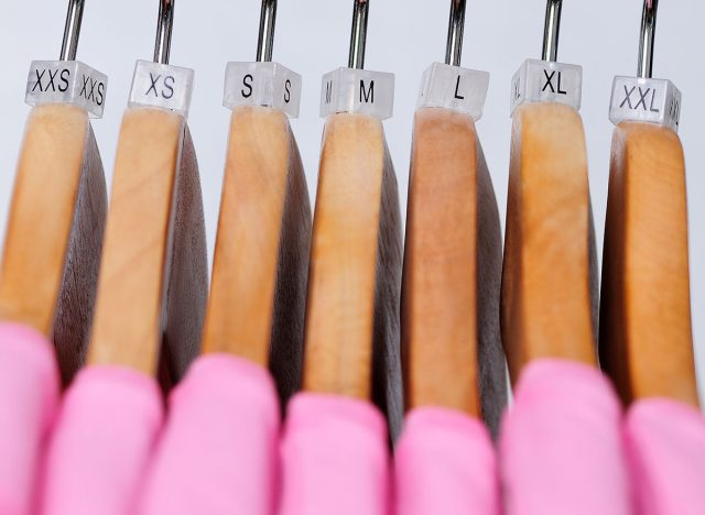 Pink women's t-shirts hang on wooden hangers with indexes of the XXS, XS, S, M, L, XL, XXL sizes on a light background.