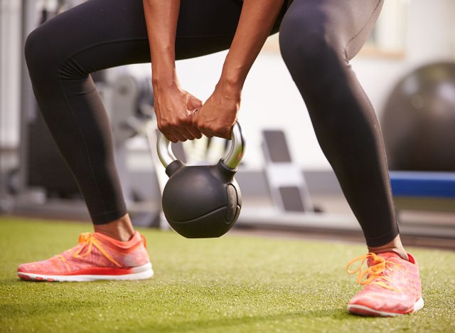 Woman exercising with a kettlebell weight, low-section crop