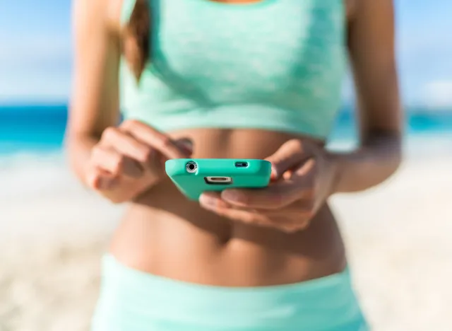 Athlete using mobile phone app fitness tracker for tracking weight loss progress during running exercise. Fit girl woman touching smartphone texting or playing online games or video workouts.