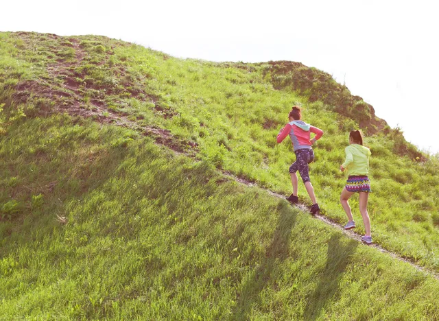 Two fit young women friends exercising in a park running up the hill. Active healthy lifestyle and outdoor workout concept