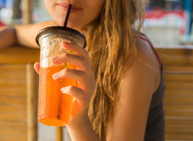 drinks, people and lifestyle concept - close up of woman drinking ice tea from plastic cup with straw at cafe. Selective focus.