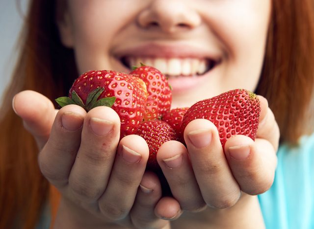 Beautiful young woman on a gray background holds a strawberry.