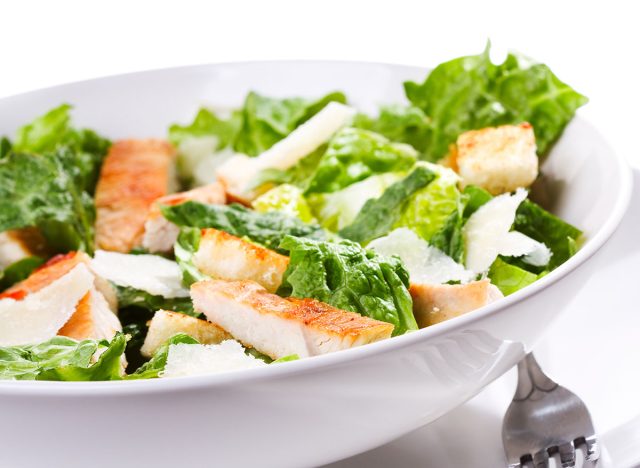 Caesar salad with chicken and greens on white background