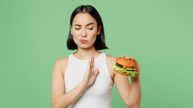 Young sad woman wear white clothes hold eat burger show hand stop gesture say "no."