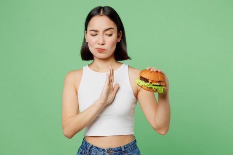 Young sad woman wear white clothes hold eat burger show hand stop gesture say "no."