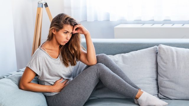 View of young woman suffering from stomachache on sofa at home