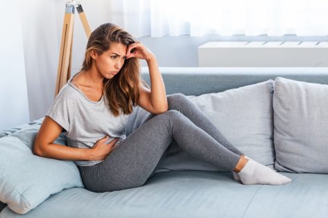 View of young woman suffering from stomachache on sofa at home