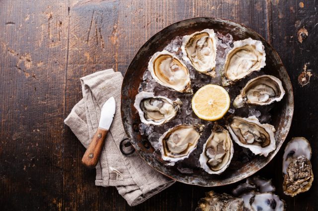 Opened Oysters on metal copper plate on dark wooden background.