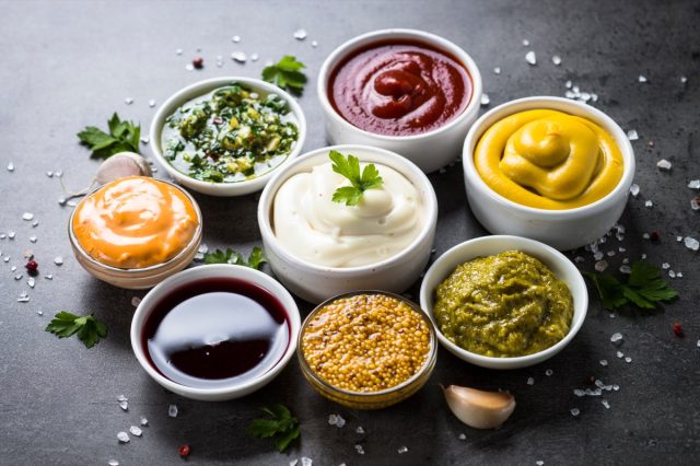 Set of sauces - ketchup, mayonnaise, mustard soy sauce, bbq sauce, pesto, chimichurri, mustard grains and pomegranate sauce on dark stone background.