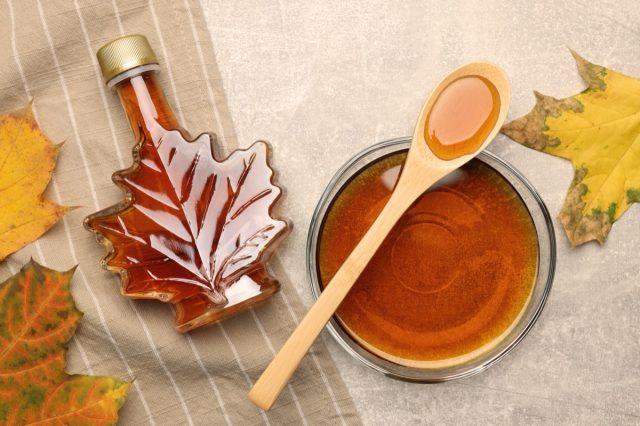 Flat lay composition with maple syrup and dry leaves on light grey table.