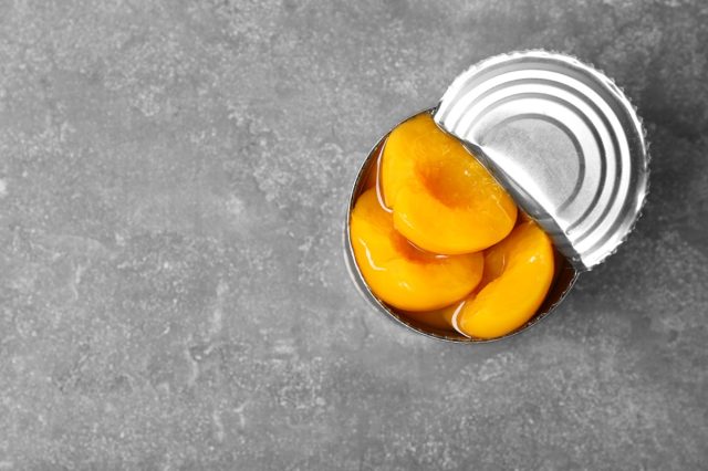 Tin can with conserved peaches on grey background, top view.