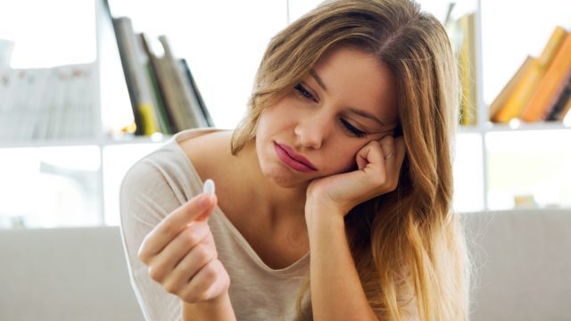 Portrait of depressed young woman taking pills at home.