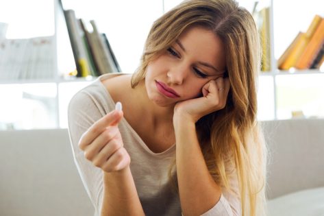 Portrait of depressed young woman taking pills at home.