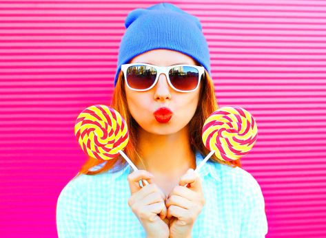 sweet woman holds two a lollipops is having fun on colorful pink background