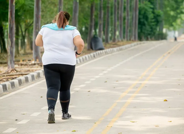 Rear view of overweight woman wearing sportswear while jogging on the road