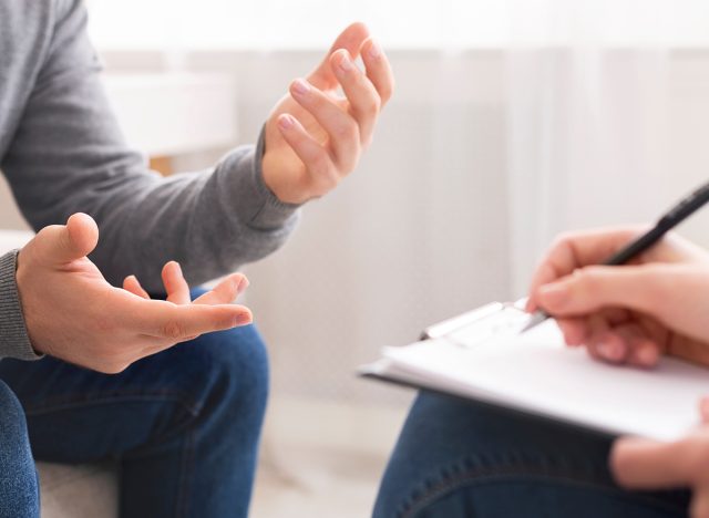 Psychotherapist writing notes, assessing patient's health and giving diagnosis to man sitting on couch during counseling session , panorama, free space