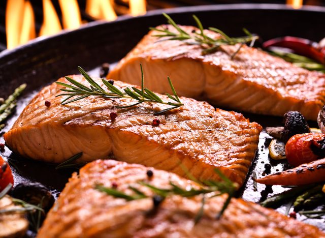 Grilled salmon fish with various vegetables on pan on the flaming grill