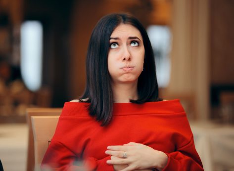 Woman Suffering a Stomachache after Eating in a Restaurant. Girl with hands on her abdomen suffering after eating too much