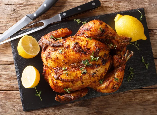 Homemade chicken rotisserie with thyme, lemon closeup on a slate board on the table. Horizontal top view from above