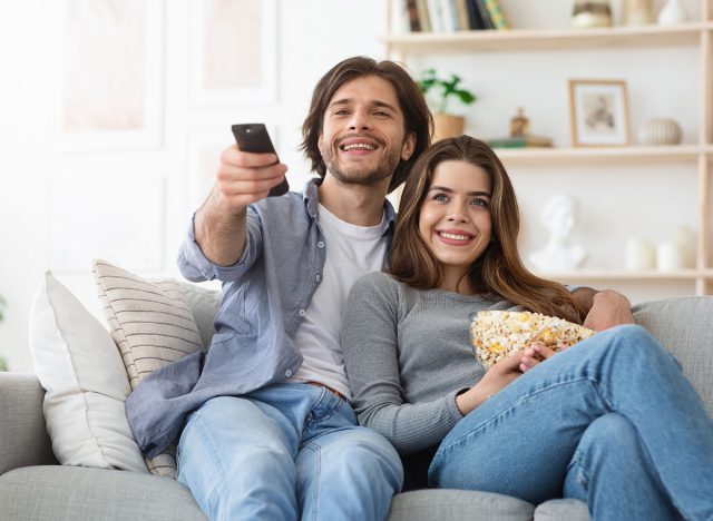 Watching TV at home. Loving couple resting on sofa and eating popcorn, copy space