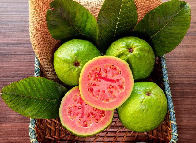 Closeup of a red guava cut in half, in the background several guavas and green leaf