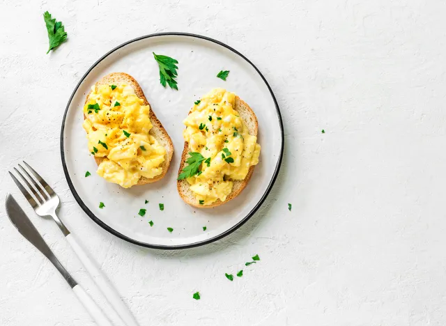 Scrambled Eggs on toasted bread for healthy breakfast or brunch on white background, top view, copy space.