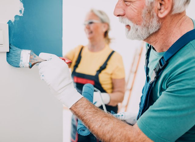 Happy senior couple renovating their home. They are painting a wall together.