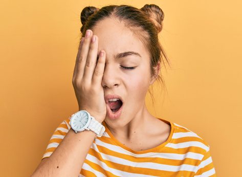 Beautiful brunette little girl wearing casual striped t shirt yawning tired covering half face, eye and mouth with hand. face hurts in pain.