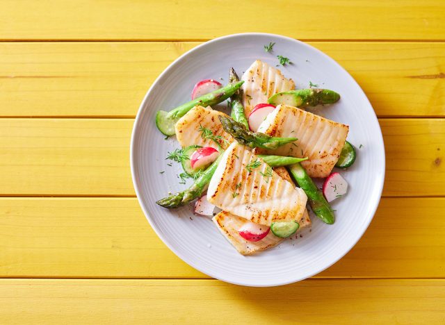 Top view of palatable grilled tilapia fish with cut vegetables served on plate on wooden table