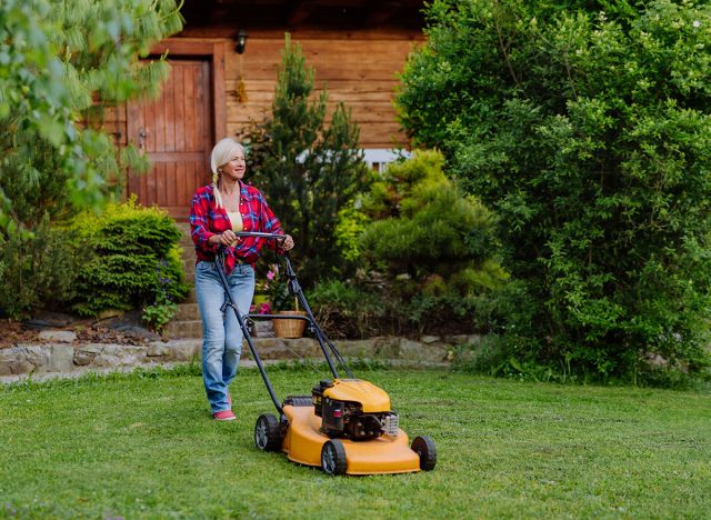 Elderly woman mowing grass with lawn mower in the garden, garden work concept.