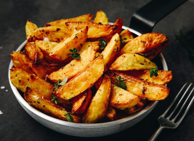 Roasted potatoes. Baked potato wedges in frying pan on dark stone background.