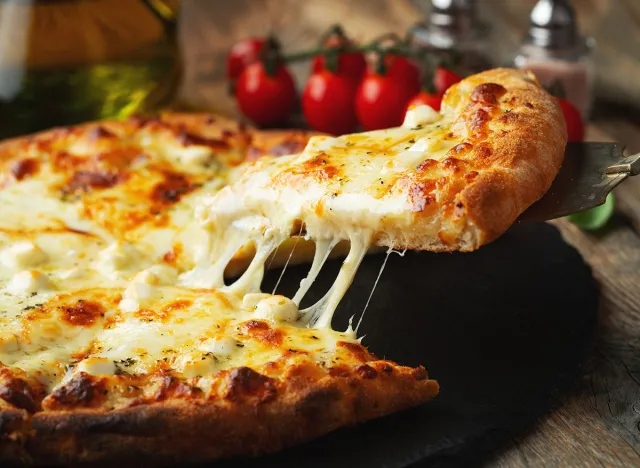 A slice of hot Italian pizza with stretching cheese. Pizza four cheeses with basil.