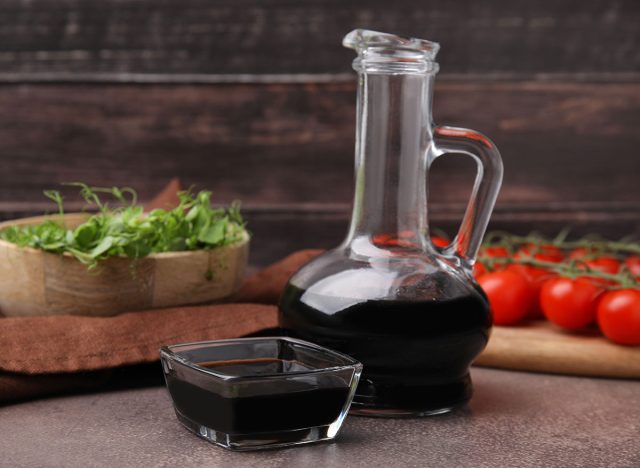 Organic balsamic vinegar, tomatoes and greens on grey table