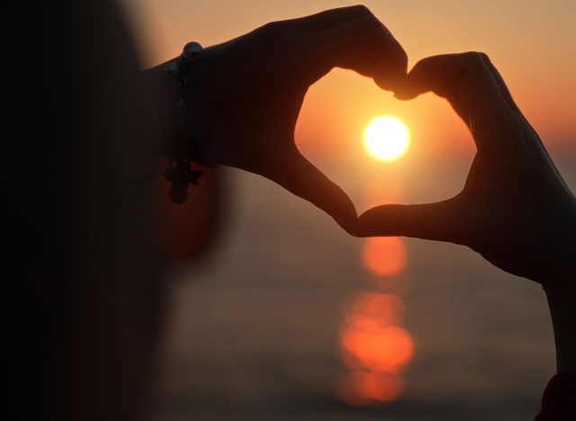 Female hands making heart shape in the sunset.