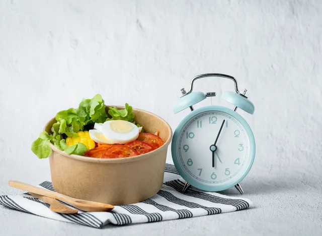 Fresh healthy salad with an alarm clock for the concept of food, time management, diet and heathy eating concept